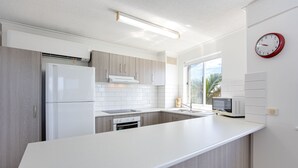 A modern kitchen with a large island, white cabinetry, and a microwave. - Coral Sea Apartments (Maroochydore)