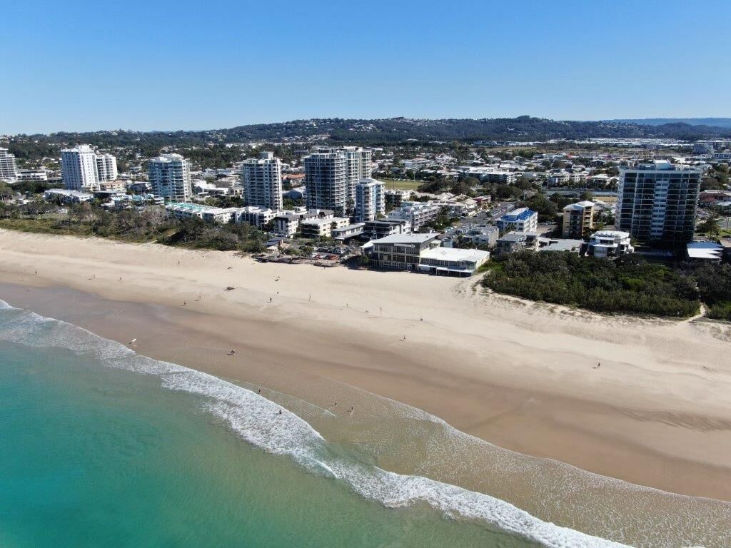 A coastal cityscape with high-rise buildings, a sandy beach, and a clear blue sky.