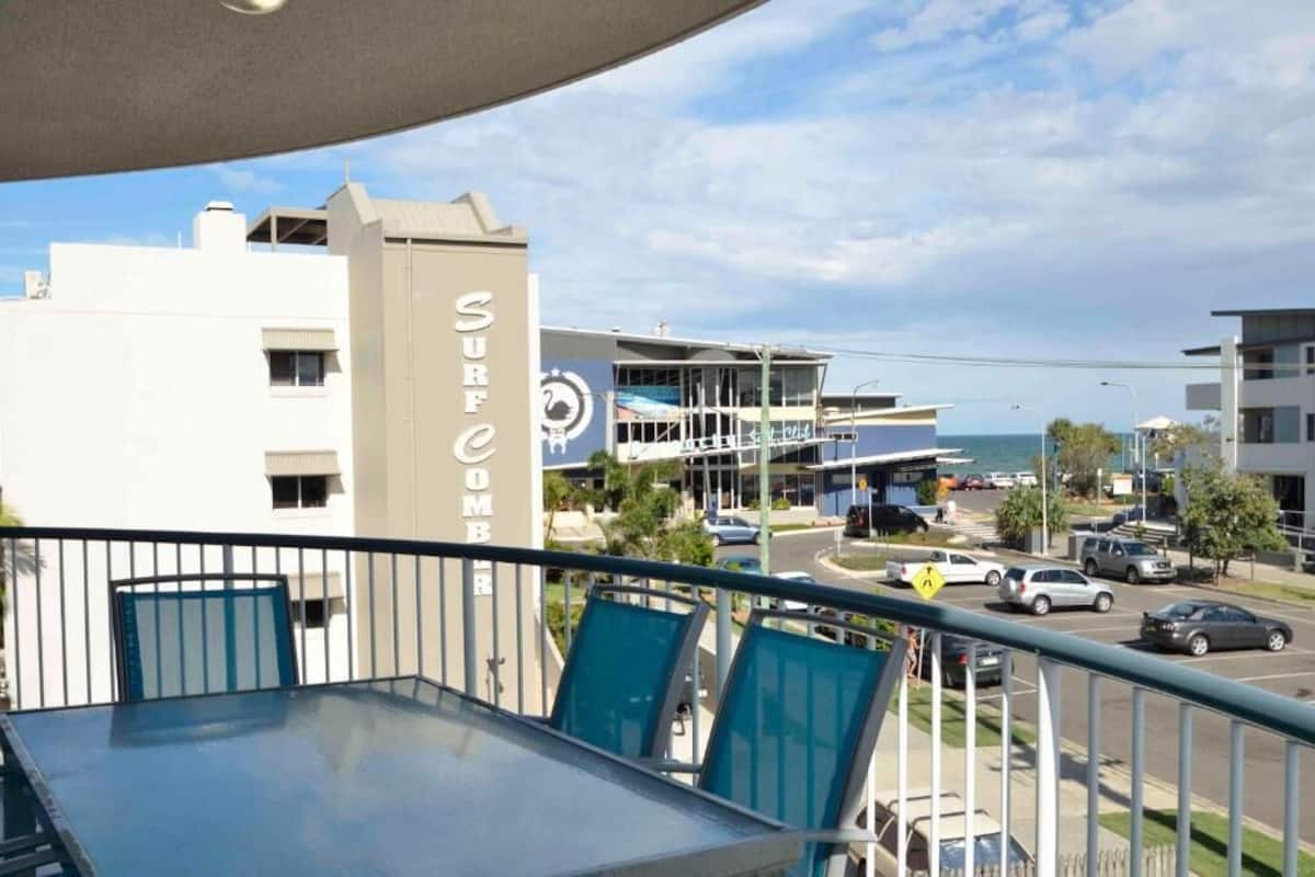 Ein Balkon mit Blick auf ein Gebäude mit der Aufschrift 'SURF COMB' und einen Parkplatz mit Autos.