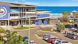 A coastal hotel with a swan logo, a parking lot, and a view of the ocean. - Coral Sea Apartments (Maroochydore)