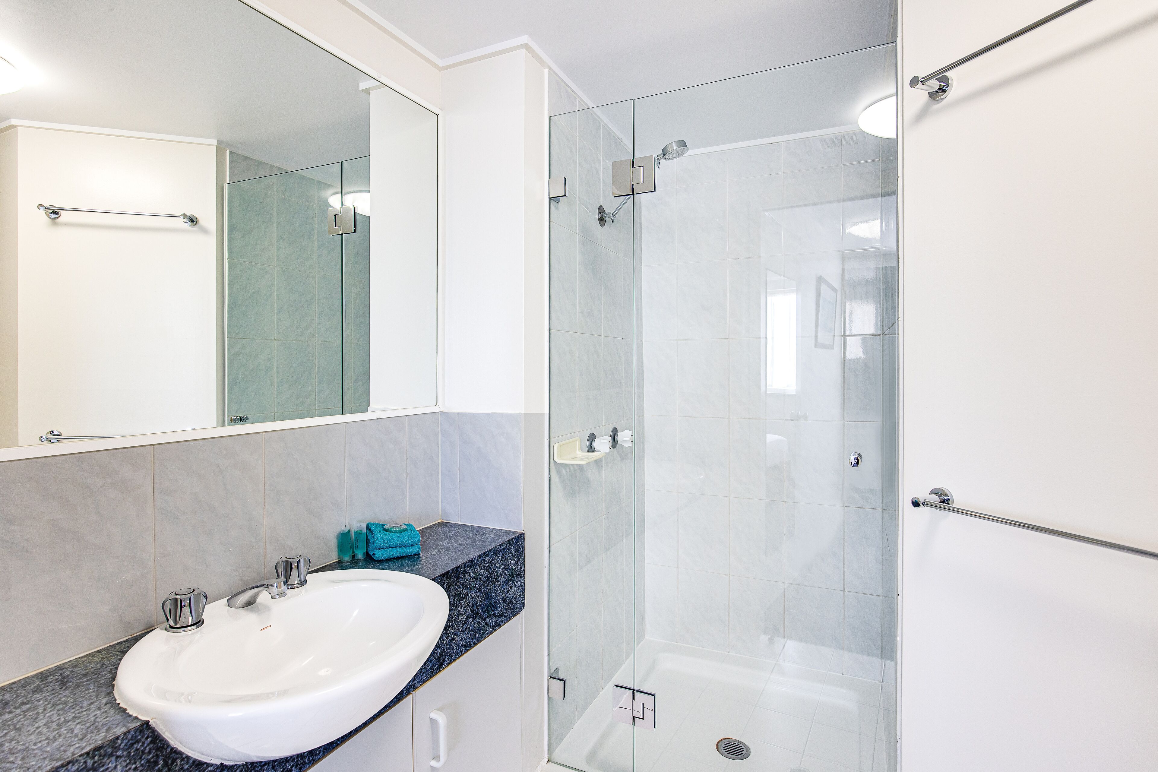 A modern bathroom with a glass-enclosed shower, a white sink, and a marble countertop.