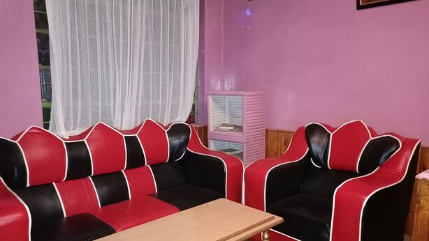 Una habitación con un sofá rojo y negro, una mesita y una pared rosa.
