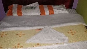 Una cama con ropa de cama blanca, almohadas a rayas y una manta con motivos florales.