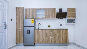 A modern kitchen with wooden cabinets, a stainless steel refrigerator, a microwave, and a sink. - Maple Homes (Accra)