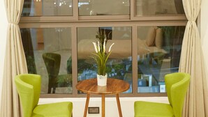 A room with a large window, two green chairs, a wooden table, and a vase with flowers. - Maple Homes (Accra)