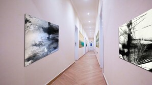 A hallway with wooden flooring, white walls, and abstract art on the walls. - Maple Homes (Accra)