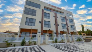 A multi-story building with a checkered pavement in front, a white fence, and a clear sky. - Maple Homes (Accra)