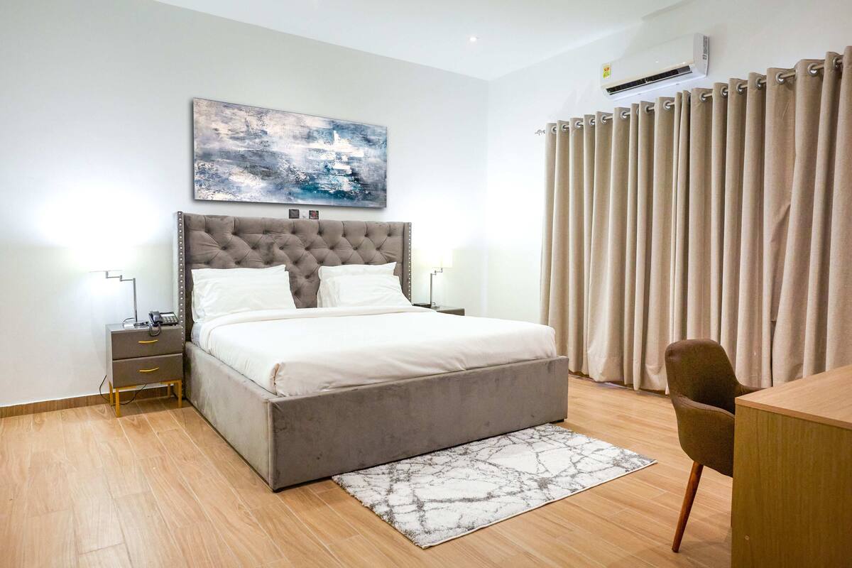 A bedroom with a large bed, bedside tables, a desk, and a chair.