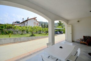 A covered outdoor area with a table and chairs, a door, and a view of a street and houses in the background.