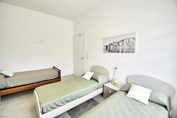 A room with two single beds, a small bedside table with a lamp, and a wall-mounted picture.