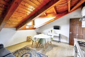 Ein gemütliches Dachzimmer mit Esstisch, Stühlen, einem kleinen Hocker, einem Fernseher und einem Herd.