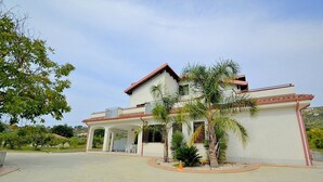 A two-story house with a covered patio and palm trees. - Villa Olga E: A cozy and welcoming apartment that is part of a villa situated in a quiet location, a few minutes from the town center, with Free WI-FI. (Agropoli)