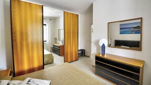 Une chambre d’hôtel avec un lit, une armoire en bois, une table de chevet, un miroir et un tableau accroché au mur.