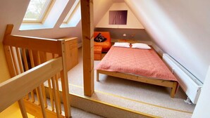 Un dormitorio con techo inclinado, una cama, una mesita de noche y un ventanal.