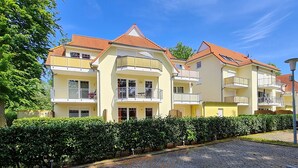 Un edificio residencial de varios pisos con balcones, un camino de entrada adoquinado y setos bien cuidados.