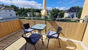 A balcony with two chairs and a table, a yellow umbrella, and a view of houses in the background.