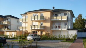 A multi-story residential building with balconies, a paved driveway, and a satellite dish.