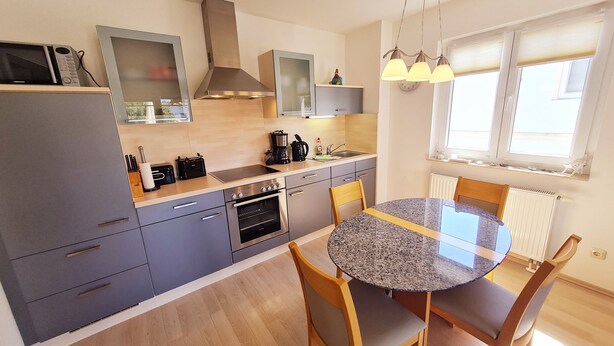A modern kitchen with grey cabinets, a built-in oven, a microwave, and a coffee maker. There is a round table with chairs in the center.