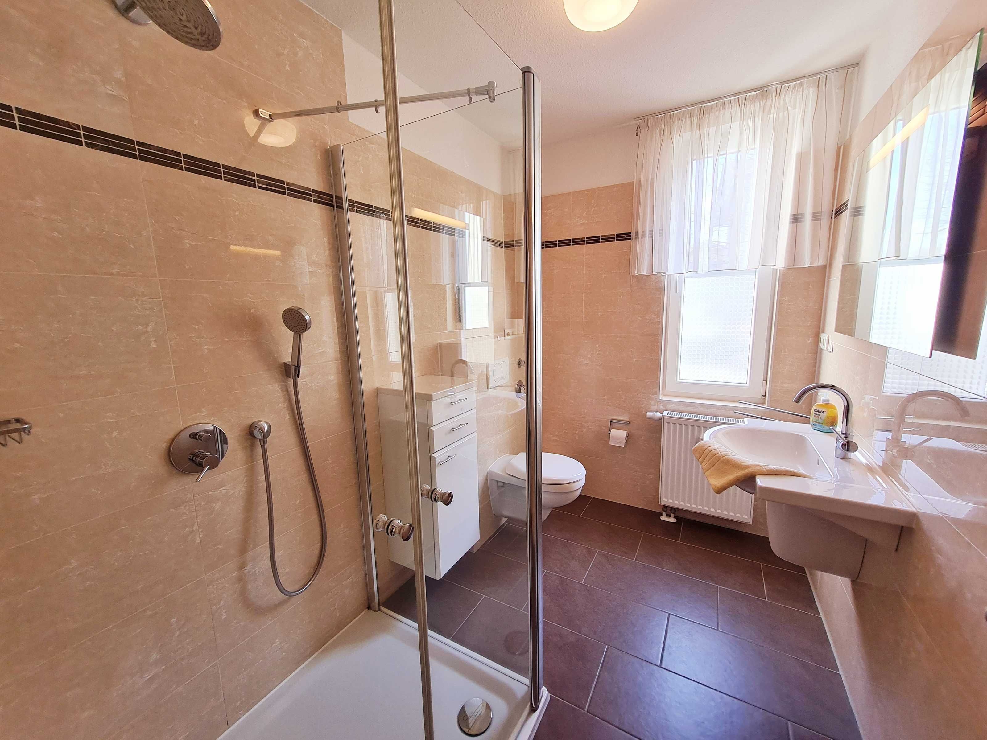 Une salle de bain moderne avec une douche à parois de verre, des toilettes blanches et un lavabo surmonté d’un miroir.