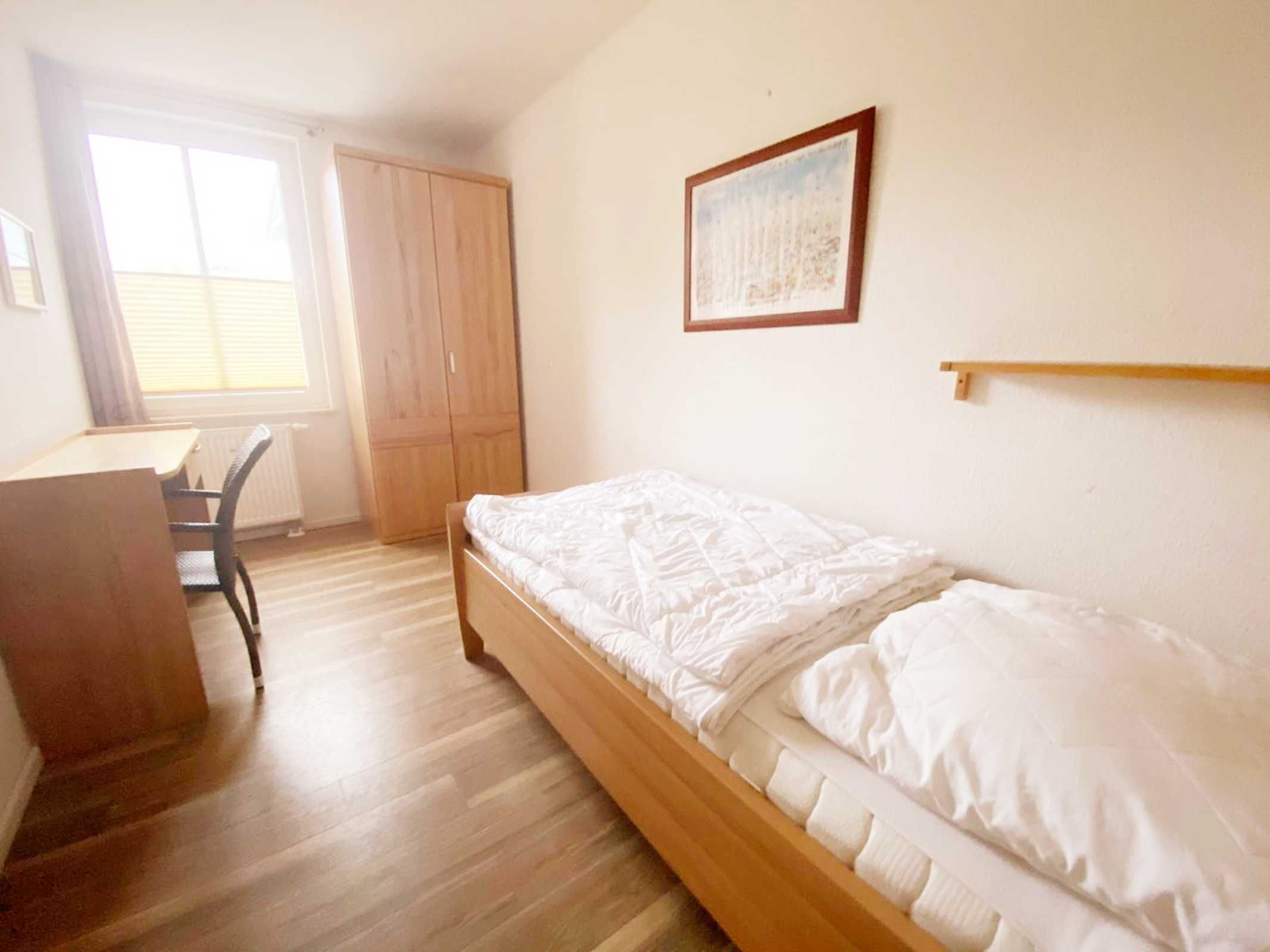 A bedroom with a single bed, a wooden desk, and a wardrobe.