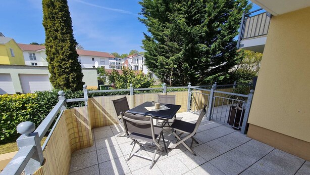 Ein Balkon mit Tisch und Stühlen, umgeben von einem Zaun und einem hohen Baum.