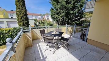 Ein Balkon mit Tisch und Stühlen, umgeben von einem Zaun und einem hohen Baum.