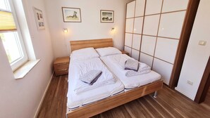 Ein Doppelbett mit Holz Kopfteil, zwei Nachttische, ein Fenster mit Jalousien und zwei gerahmte Bilder an der Wand.