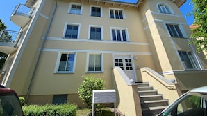 Ein mehrgeschossiges Wohnhaus mit beiger Fassade, weißem Zierdekor und einem Balkon auf der linken Seite.