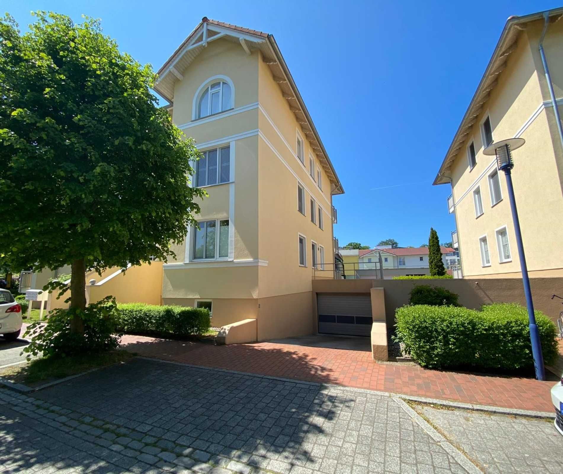 Un edificio residencial de varios pisos con fachada beige, entrada central y camino de entrada pavimentado.