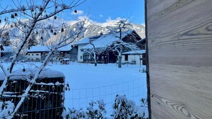 Un pueblo nevado con casas de madera tradicionales, una zona vallada y montañas al fondo.