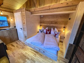 A wooden interior with a bed, two wall-mounted lights, and a window. - Tinyhouse - Alpenapart Singer (Ehenbichl)