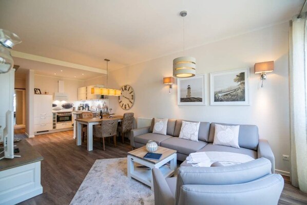 Un salon moderne avec un canapé, une table basse et un coin repas. Il y a une horloge au mur et une lampe au-dessus du canapé.