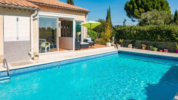 A swimming pool with a clear blue water, a covered patio with outdoor furniture, and a view of the surrounding greenery. - Peaceful Escape in Argeliers (Argeliers)