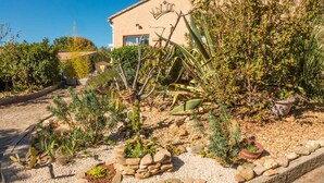 A garden with various plants and a stone pathway leading to a building with a sign that reads "WOC". - Peaceful Escape in Argeliers (Argeliers)