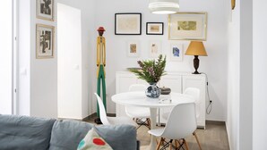 A dining area with a white table, chairs, a vase with flowers, and framed artwork on the wall.