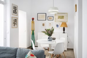 A dining area with a white table, chairs, a vase with flowers, and framed artwork on the wall.