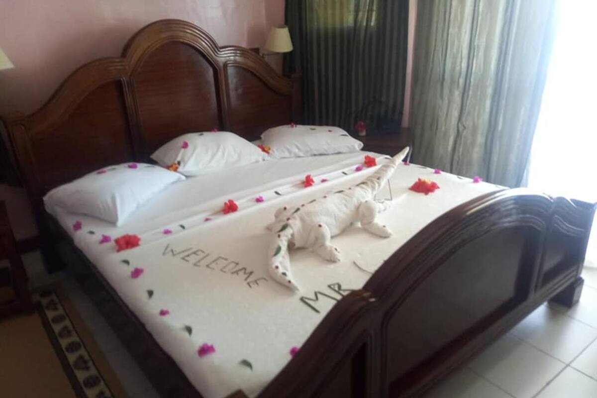 Una cama bien hecha con un tapete de bienvenida, almohadas y un peluche decorativo.