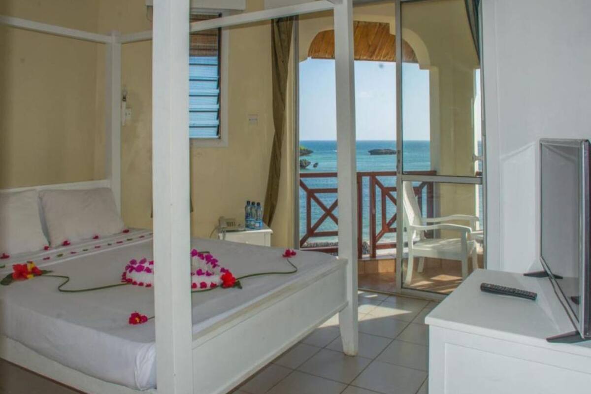 Habitación de hotel con cama, televisión y balcón con vistas al mar.