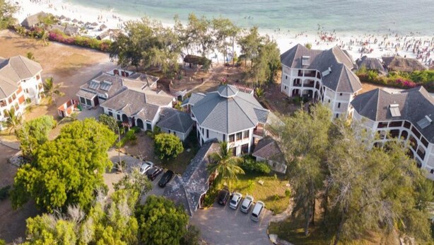 Vista aérea de un resort con varias construcciones, un estacionamiento y una playa al fondo.