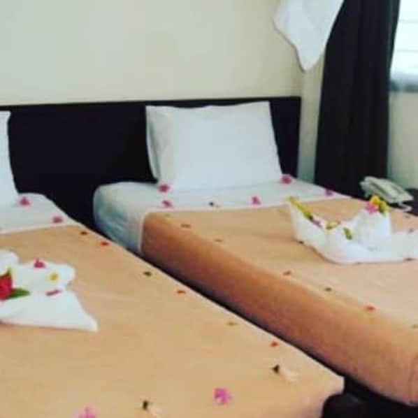 Habitación de hotel con dos camas, cada una con un almohadón blanco y un arreglo floral.