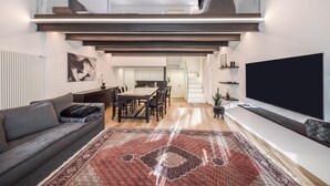 Ein modernes Wohnzimmer mit einer Couch, einem Essbereich, einer Treppe und einem an der Wand befestigten Fernseher.