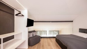 Ein modernes Schlafzimmer mit Bett, Sofa, Fernseher und einem Fenster mit Vorhängen.