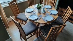 A dining area with a round table set for four, surrounded by wooden chairs with grey cushions. - Family friendly, 3 bedrooms with parking & garden. Close to beach and town. (Bridlington)