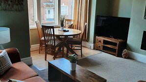 A living room with a sofa, a coffee table, a TV, and a dining area with chairs and a table. - Family friendly, 3 bedrooms with parking & garden. Close to beach and town. (Bridlington)