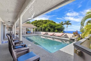 A pool area with lounge chairs, a clear view of the ocean, and a tropical setting with palm trees. - Breathtaking Panoramic Ocean Views, Crystal Blue Pool, Hot Tub, BBQ Grill! (Kailua-Kona)