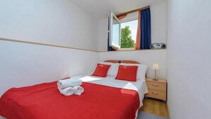 Ett hotellrum med en säng, ett nattduksbord, en lampa, en radio och ett fönster med gardiner.