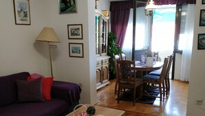 Ett vardagsrum med en lila soffa, ett träbord som soffbord och en matplats med ett bord och stolar.