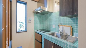 A compact kitchen with teal tiles, a stainless steel sink, and wooden cabinets.