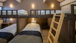 A dormitory room with bunk beds, wooden beams, and wall-mounted lights.