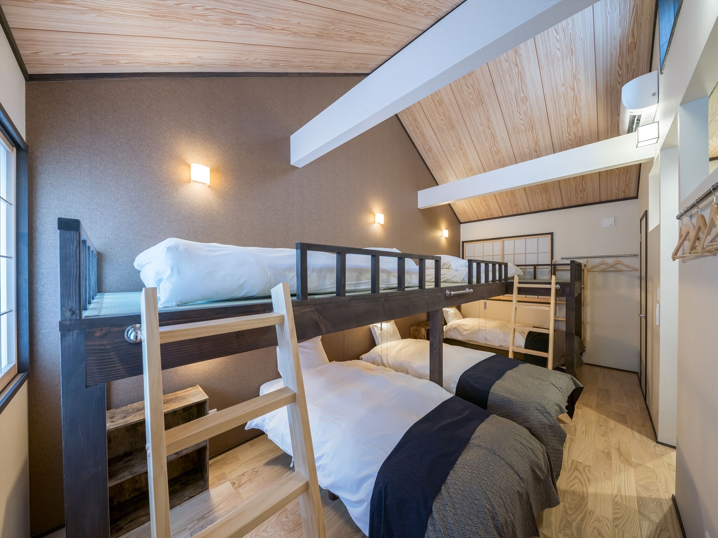 A dormitory room with bunk beds, a wooden staircase, and a ceiling with exposed beams.